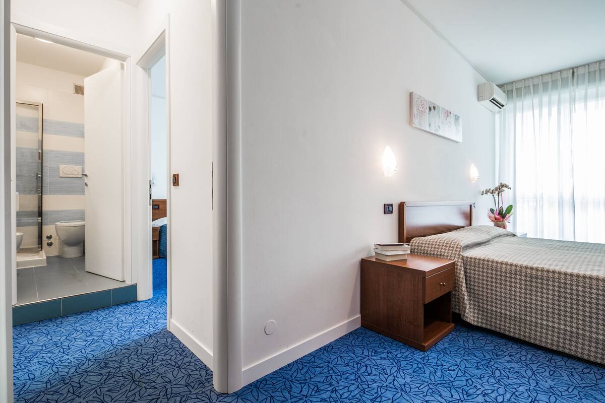 Quarto de hotel com cama, mesa de cabeceira e banheiro visível por uma porta aberta.