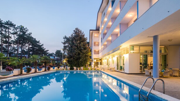 A swimming pool with a clear blue water surface, surrounded by a white building with multiple floors and balconies.