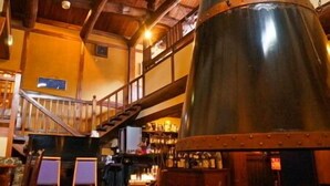 Een rustiek interieur met een grote metalen schoorsteen, houten balken, een trap en een bar met flessen.