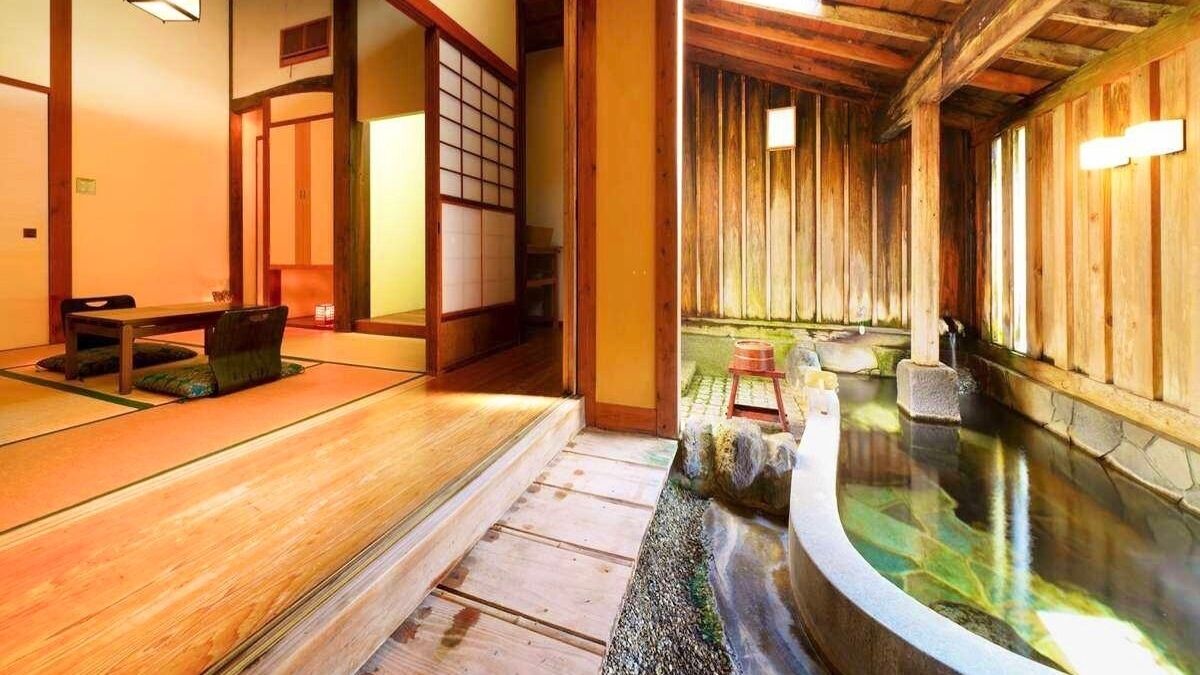 Una habitación japonesa tradicional con suelo de tatami, interior de madera y una pequeña zona de onsen (aguas termales).