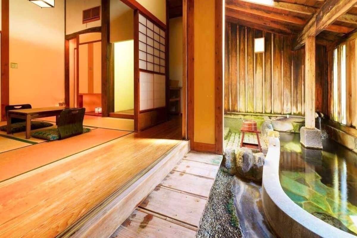 Une pièce de style japonais traditionnel, avec un sol recouvert de tatamis, un décor intérieur en bois et un petit espace aménagé en onsen (source thermale).