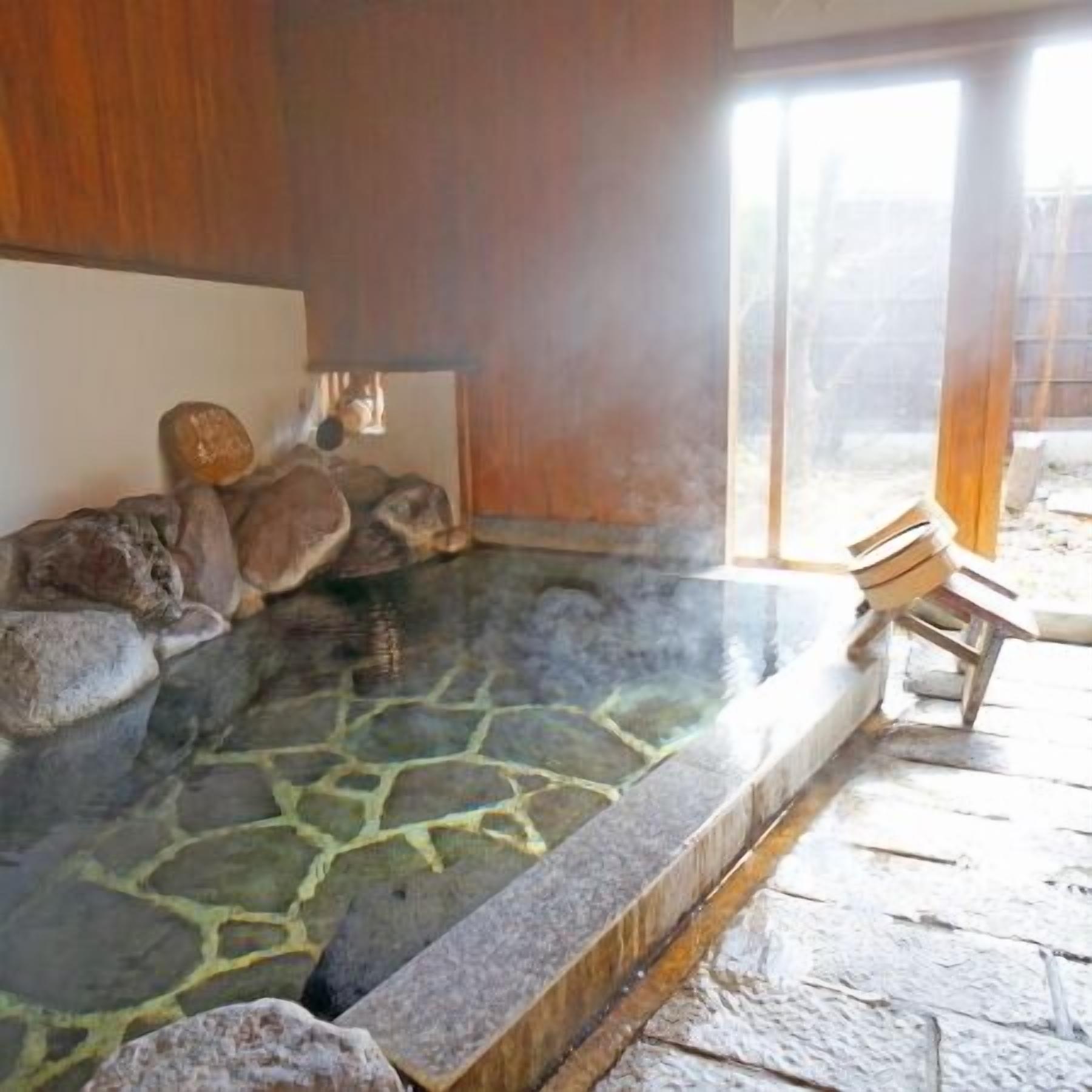 Una bañera de piedra con rocas, una silla de madera y vistas al exterior.