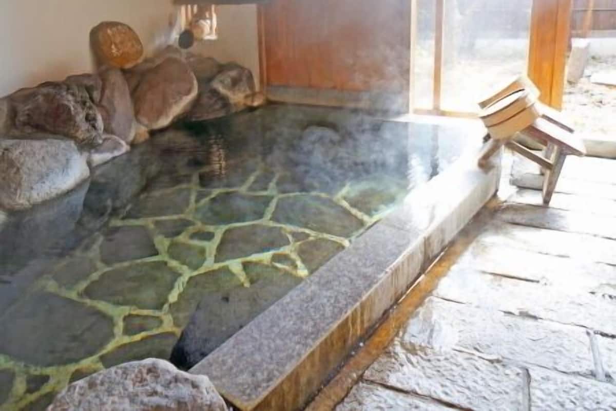 Un bain à remous en pierre avec des rochers, une chaise en bois et une vue sur l’extérieur.