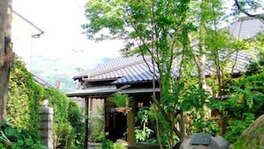Een traditioneel Japans gebouw met pannendak, omringd door weelderige begroeiing en een pad van stenen.