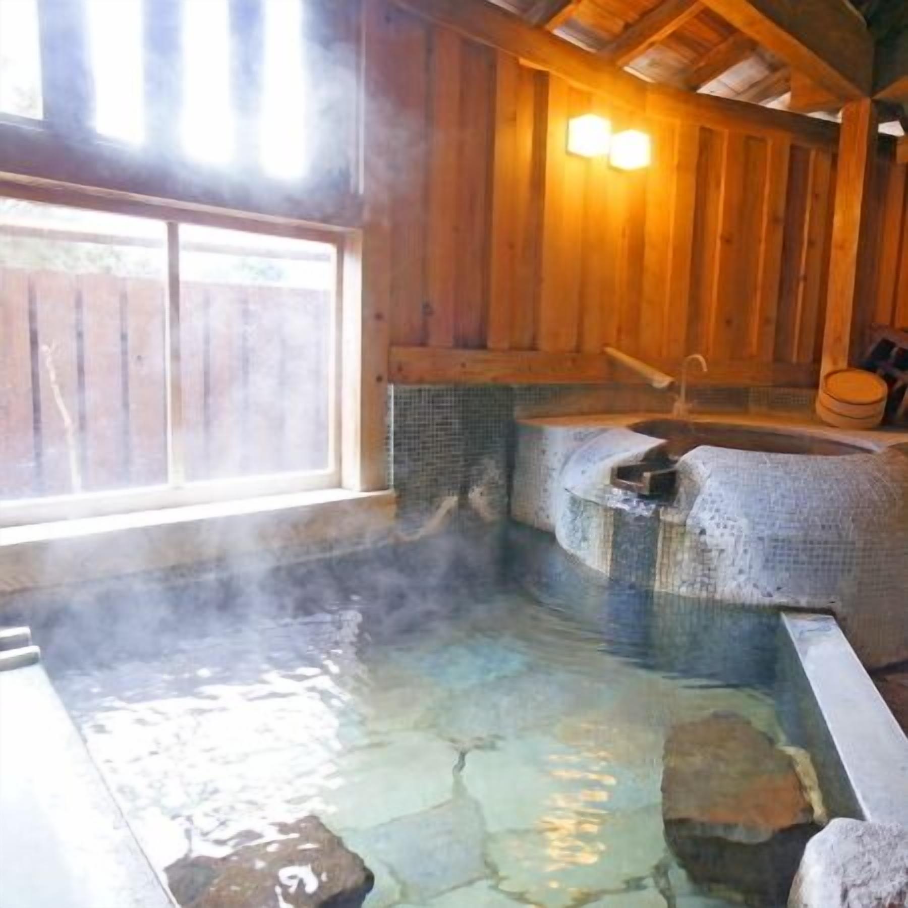Un baño de aguas termales con baldosas de piedra, paredes de madera y una ventana.