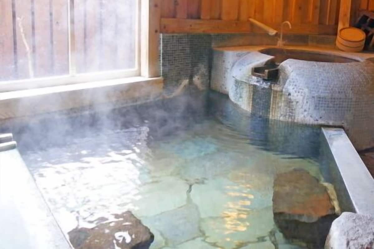 Un baño de aguas termales con baldosas de piedra, paredes de madera y una ventana.