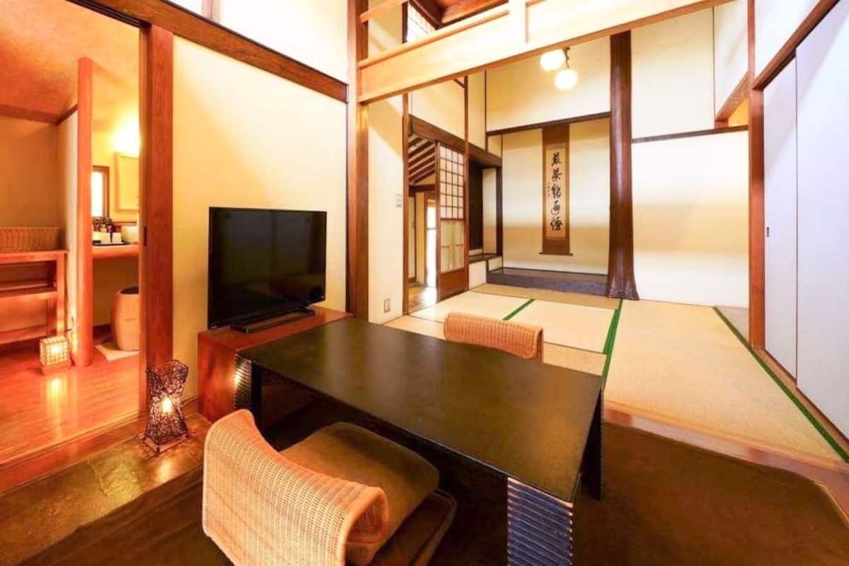 Une pièce de style japonais traditionnel, avec un sol recouvert de tatamis, une télévision, une petite table et des portes coulissantes donnant sur une autre pièce.