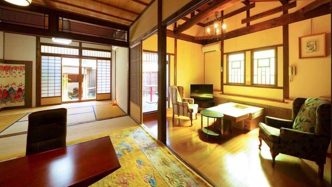 Una habitación japonesa tradicional con suelo de tatami, puertas correderas, una mesa baja, sillas y un televisor.