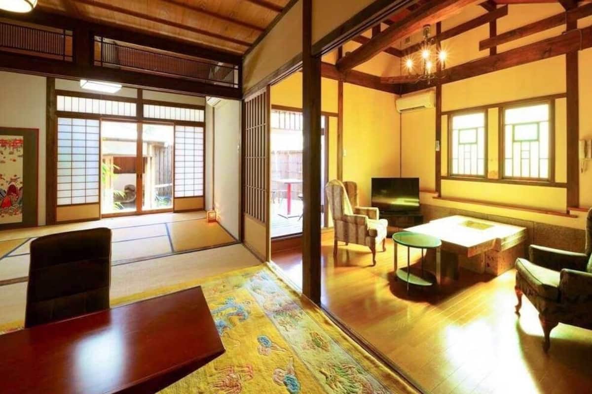 Une pièce de style japonais traditionnel, avec un sol recouvert de tatamis, des portes coulissantes, une petite table, des chaises et un téléviseur.