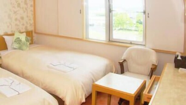 Une chambre d’hôtel avec deux lits, une petite table, une chaise et une fenêtre donnant sur un paysage verdoyant.