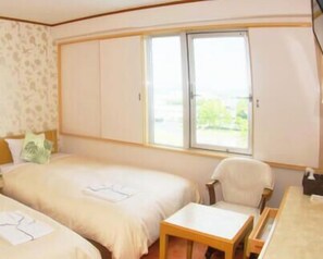 A hotel room with two beds, a small table, a chair, and a window with a view of greenery. - Central Hotel Yasu (Yasu)