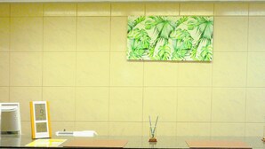 Une salle de bain avec un grand miroir, une horloge et un tableau représentant des feuilles tropicales, accroché au mur.