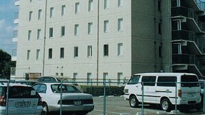 Un immeuble à étages doté d’une façade uniforme, de nombreuses fenêtres et d’une antenne visible sur le toit.