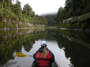 A person in a canoe on a calm river surrounded by dense forest. - Canoe Safaris Lodge (Ohakune)