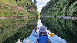 A canoeist paddling down a calm river surrounded by lush greenery. - Canoe Safaris Lodge (Ohakune)