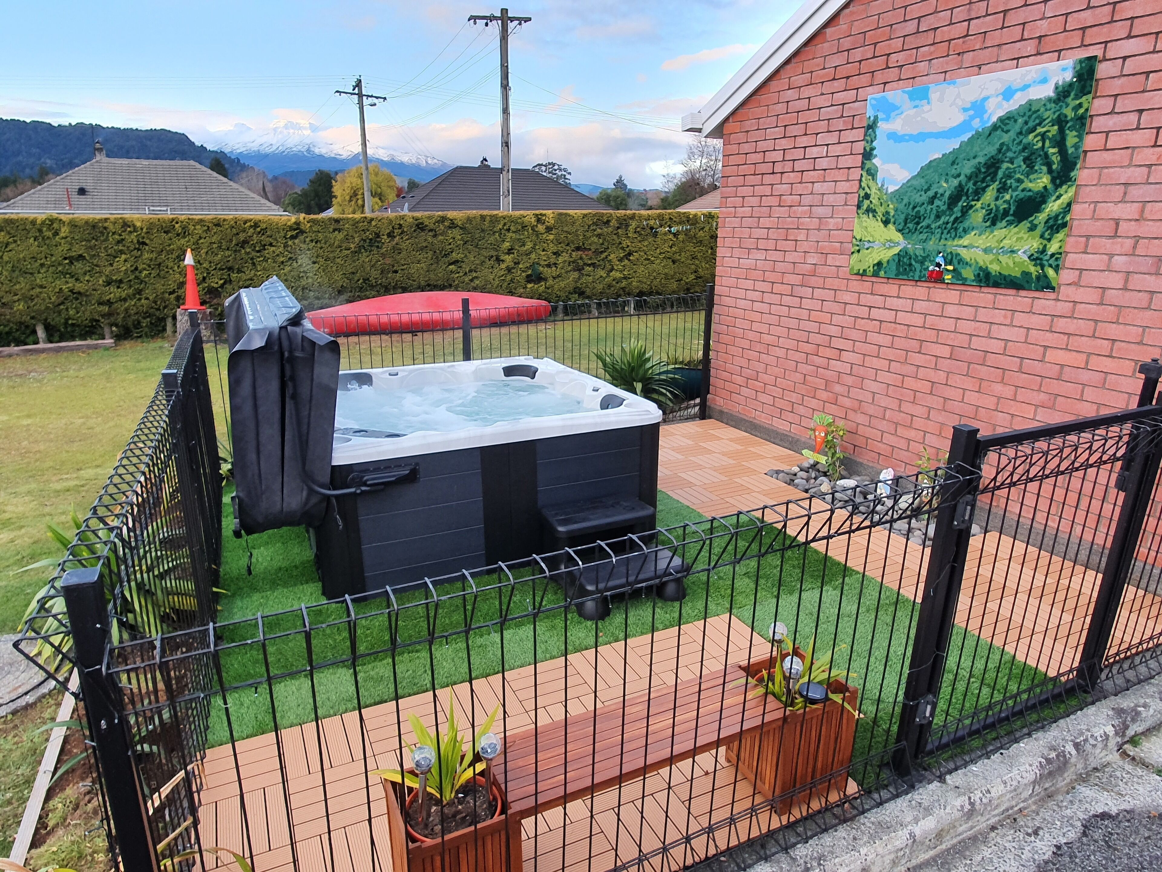 A hot tub in a fenced backyard with a painting of a landscape on the wall.