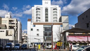 A modern building with a prominent sign at the top, surrounded by parked cars and a clear blue sky. - Hotel Zaaz (Oita)
