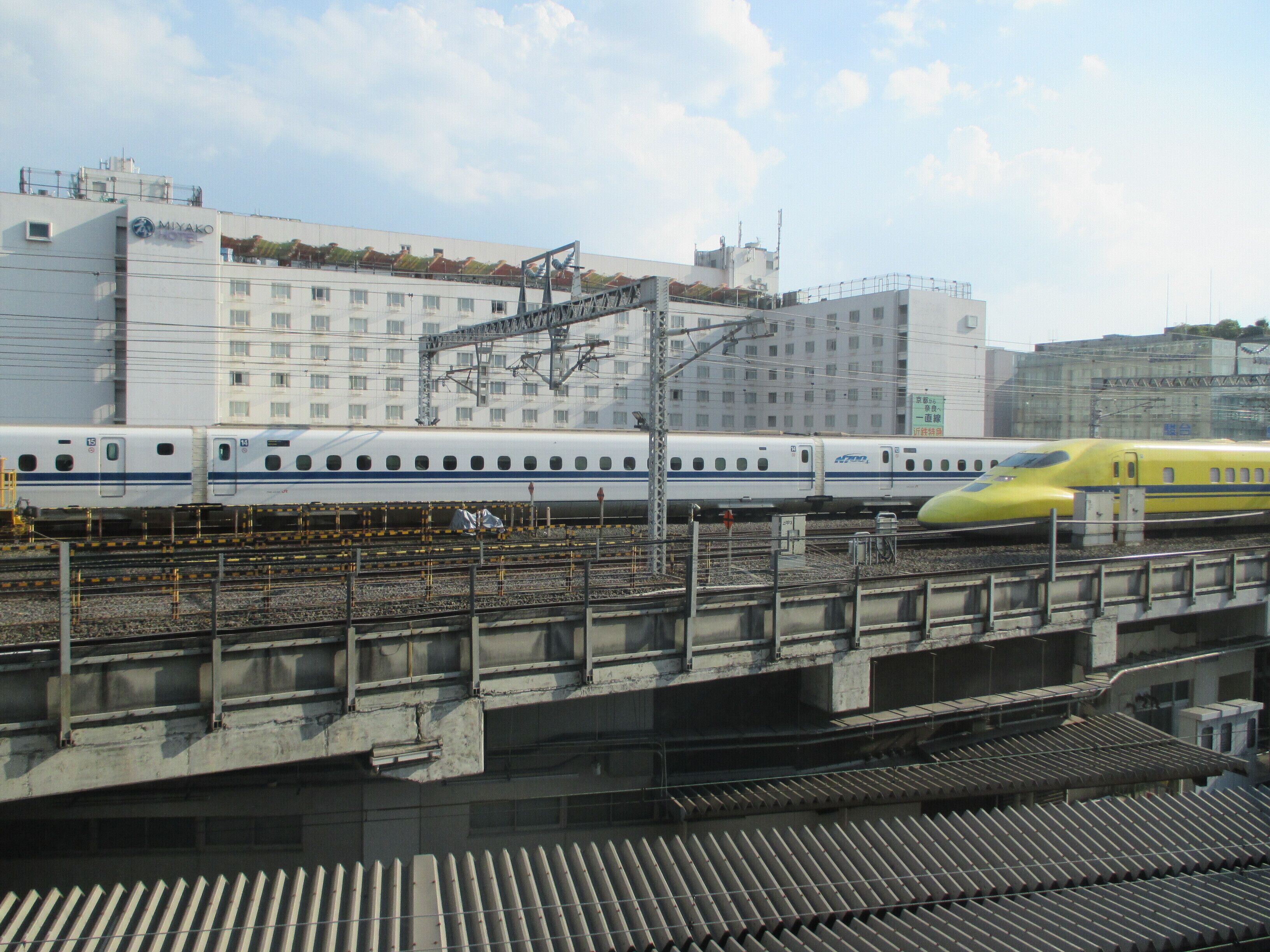 Una estación de tren con un moderno tren amarillo y un hotel al fondo.