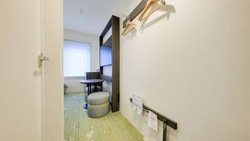 A hotel room with a small table, a bench, a towel rack, and a window with blinds.