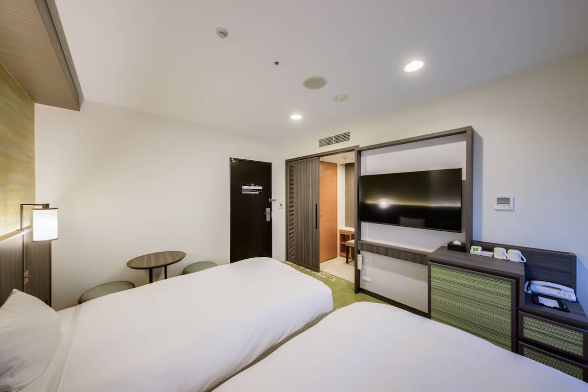 Quarto de hotel com duas camas, uma escrivaninha com telefone, televisão e uma pequena mesa com cadeiras.