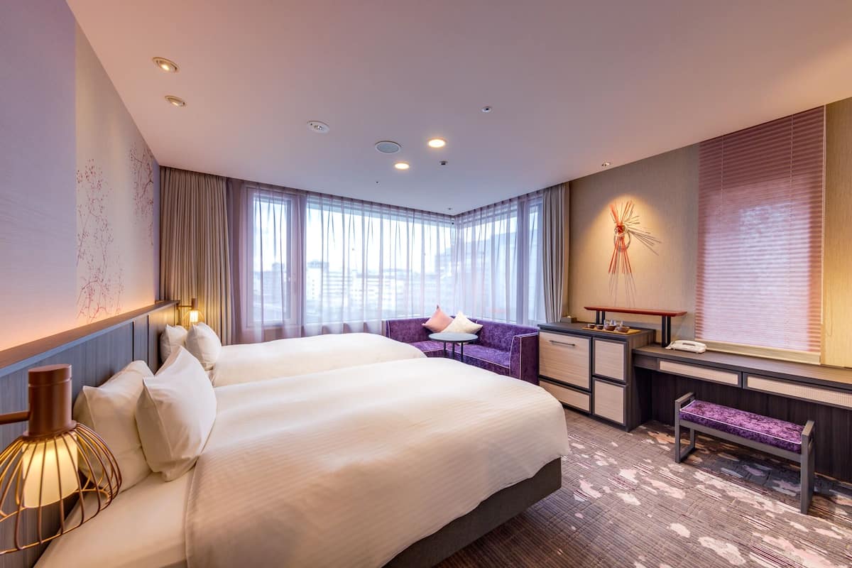 Quarto de hotel moderno com uma cama grande, uma escrivaninha, uma cadeira e um sofá.