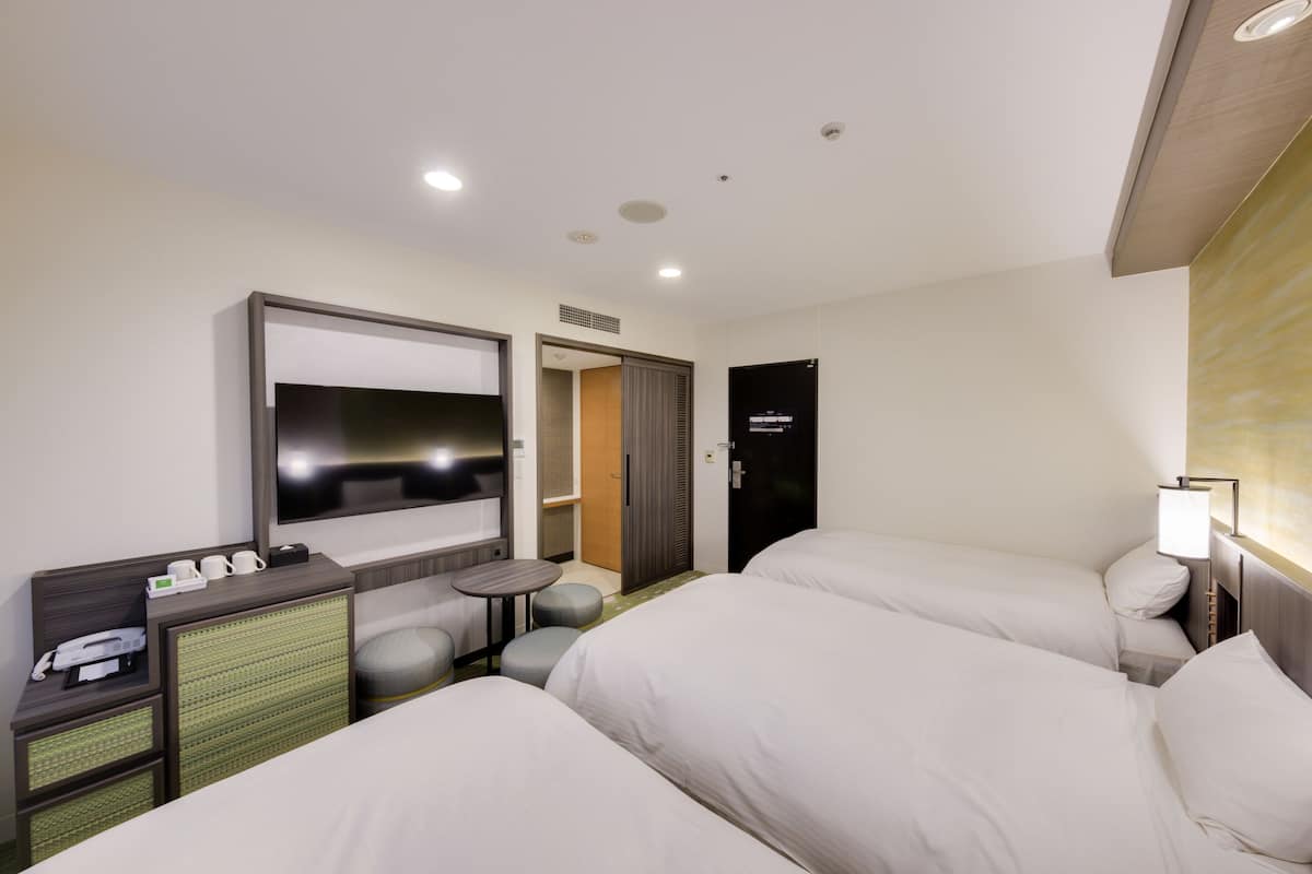 Quarto de hotel com duas camas, televisão, escrivaninha com telefone e uma mesinha.