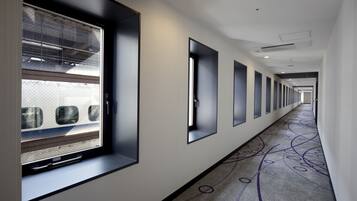 A long, narrow hotel corridor with a patterned carpet, large windows, and a modern design.