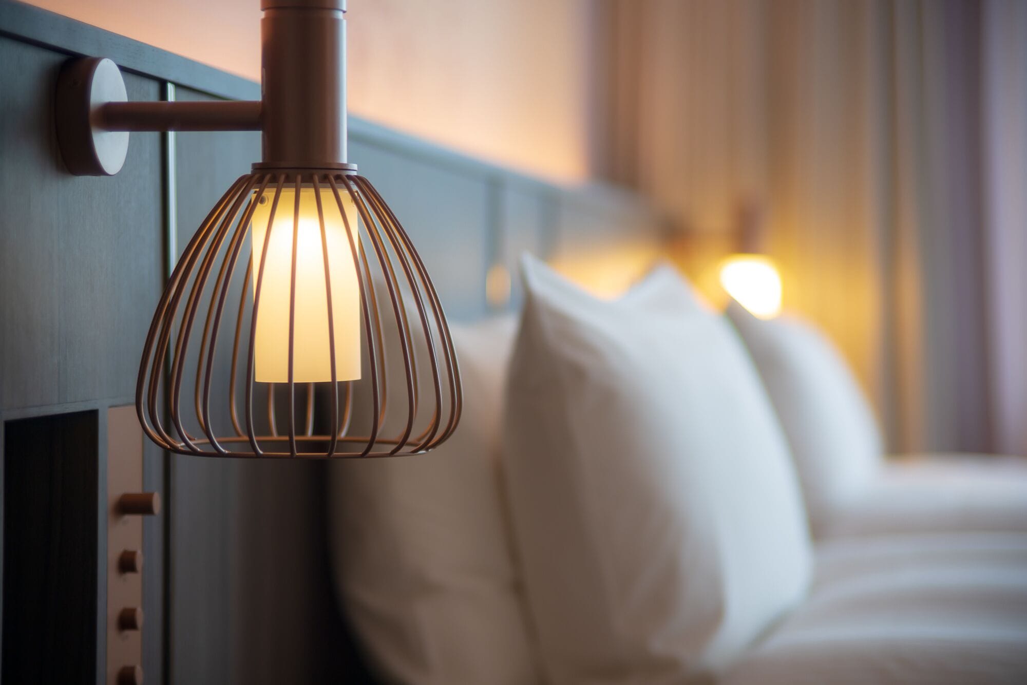 Un gros plan d’un lit avec des oreillers blancs et un luminaire suspendu doté d’un cadre en métal.