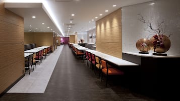 A modern dining area with long tables and chairs, wooden paneling, and recessed lighting.