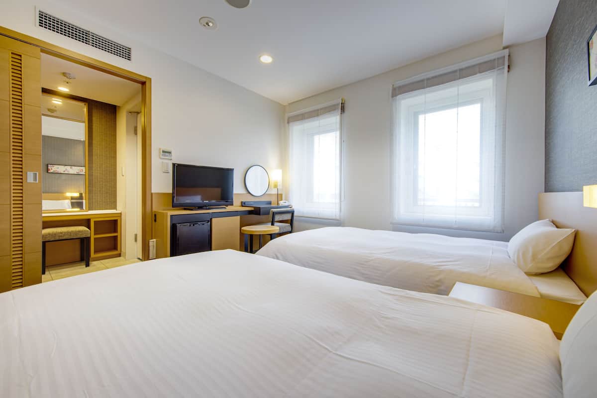 Quarto de hotel com duas camas, uma escrivaninha com computador, televisão e uma pequena mesa com cadeira.