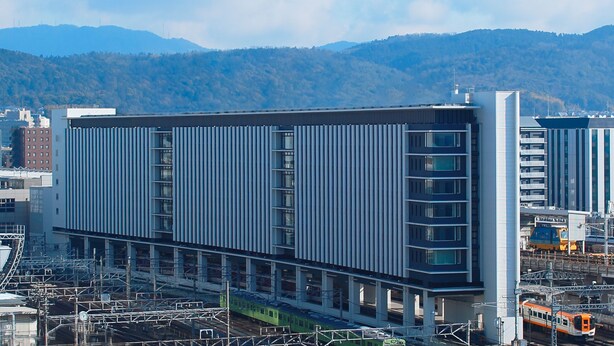 A modern building with a linear facade, multiple floors, and a train passing by. - Miyako City Kintetsu Kyoto Station (Kyoto)