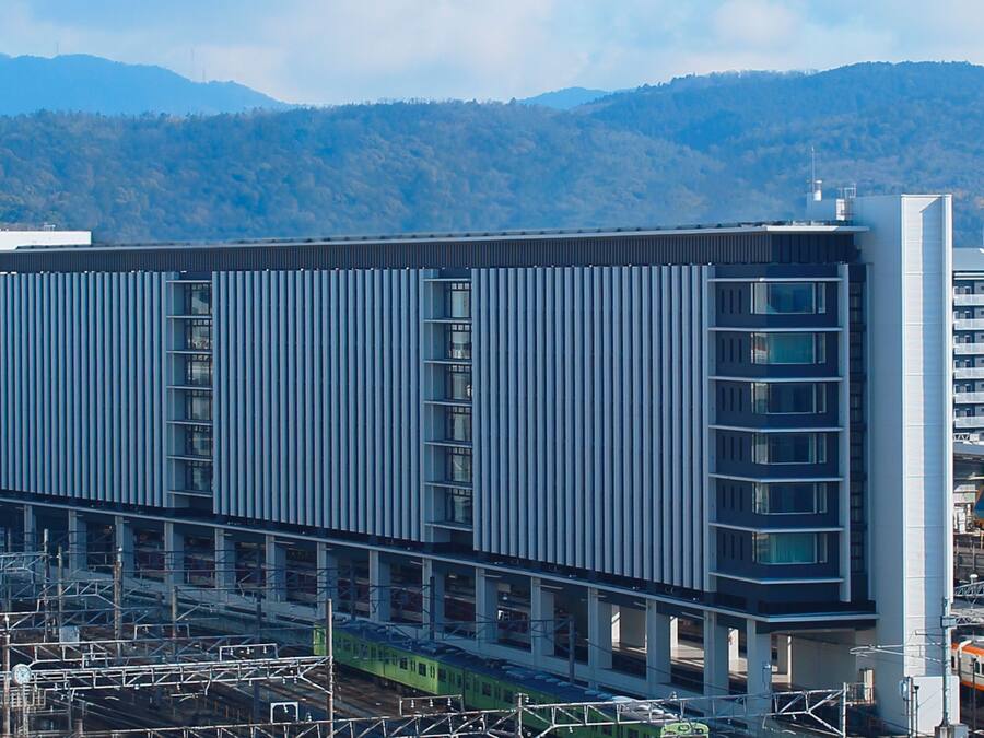 A modern building with a linear facade, multiple floors, and a train passing by.