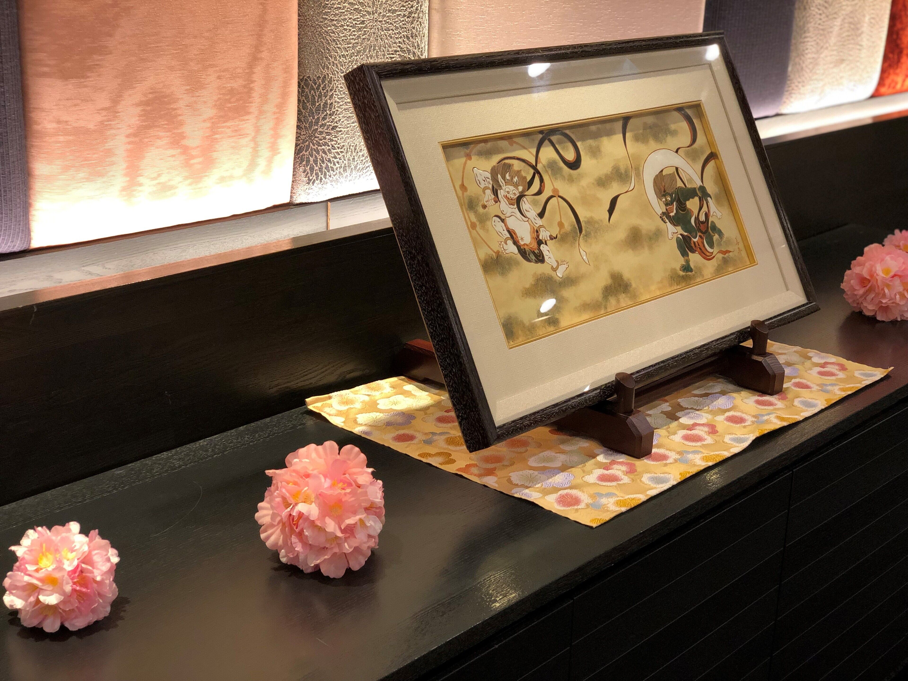 Une œuvre d’art encadrée est posée sur une étagère en bois foncé, et un tissu à motifs se trouve en dessous.