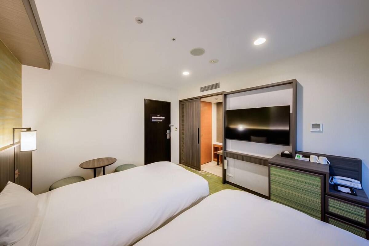 Quarto de hotel com duas camas, uma escrivaninha, televisão de tela plana, uma mesinha e uma cadeira.
