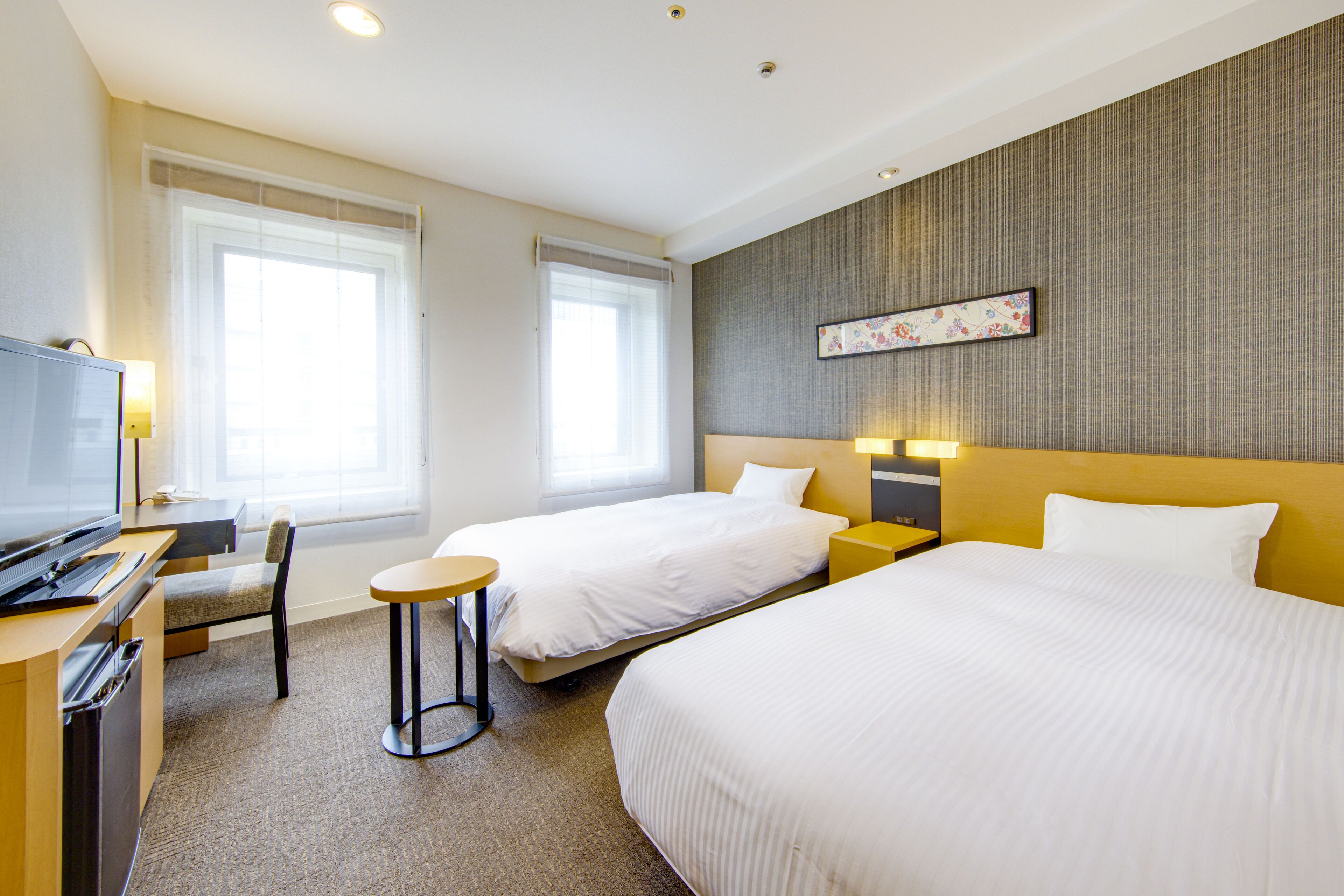 A hotel room with two beds, a desk, a chair, a TV, and a small table.