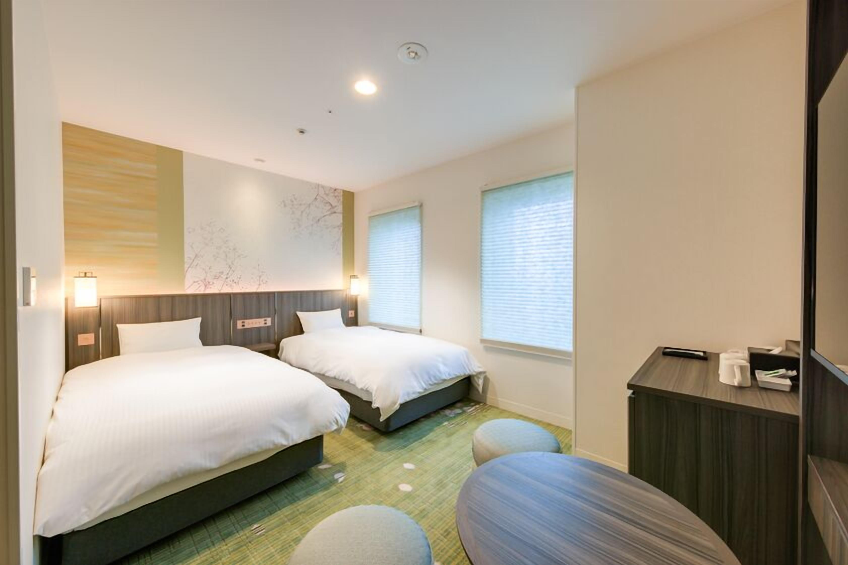 A hotel room with two beds, a desk, and a small seating area.