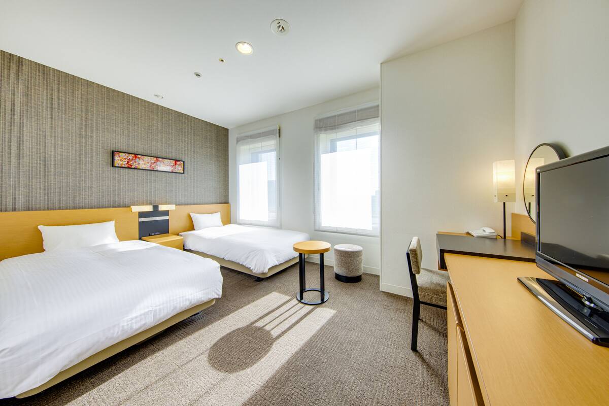 Quarto de hotel com duas camas, uma escrivaninha, uma televisão e uma mesa redonda pequena.