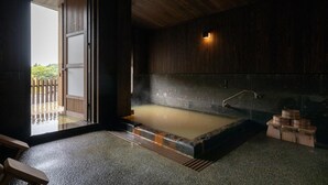 A traditional Japanese onsen with a wooden interior, a stone hot spring, and a wooden bench. - Ryokan Nanjoen (Minamioguni)