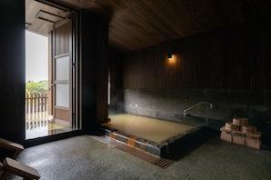 A traditional Japanese onsen with a wooden interior, a stone hot spring, and a wooden bench. - Ryokan Nanjoen (Minamioguni)