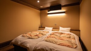 A double bed with a patterned bedspread, a bedside table with a vase, and a wall-mounted light fixture. - Ryokan Nanjoen (Minamioguni)