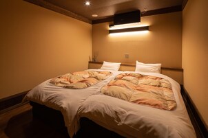 A double bed with a patterned bedspread, a bedside table with a vase, and a wall-mounted light fixture.