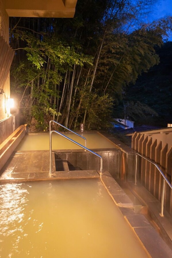 A hot spring area with a metal staircase leading down to a pool of water, surrounded by trees and a building structure. - Ryokan Nanjoen (Minamioguni)