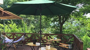 Una terrassa de fusta amb taules i cadires rodones, un hamaca i un parasol verd.