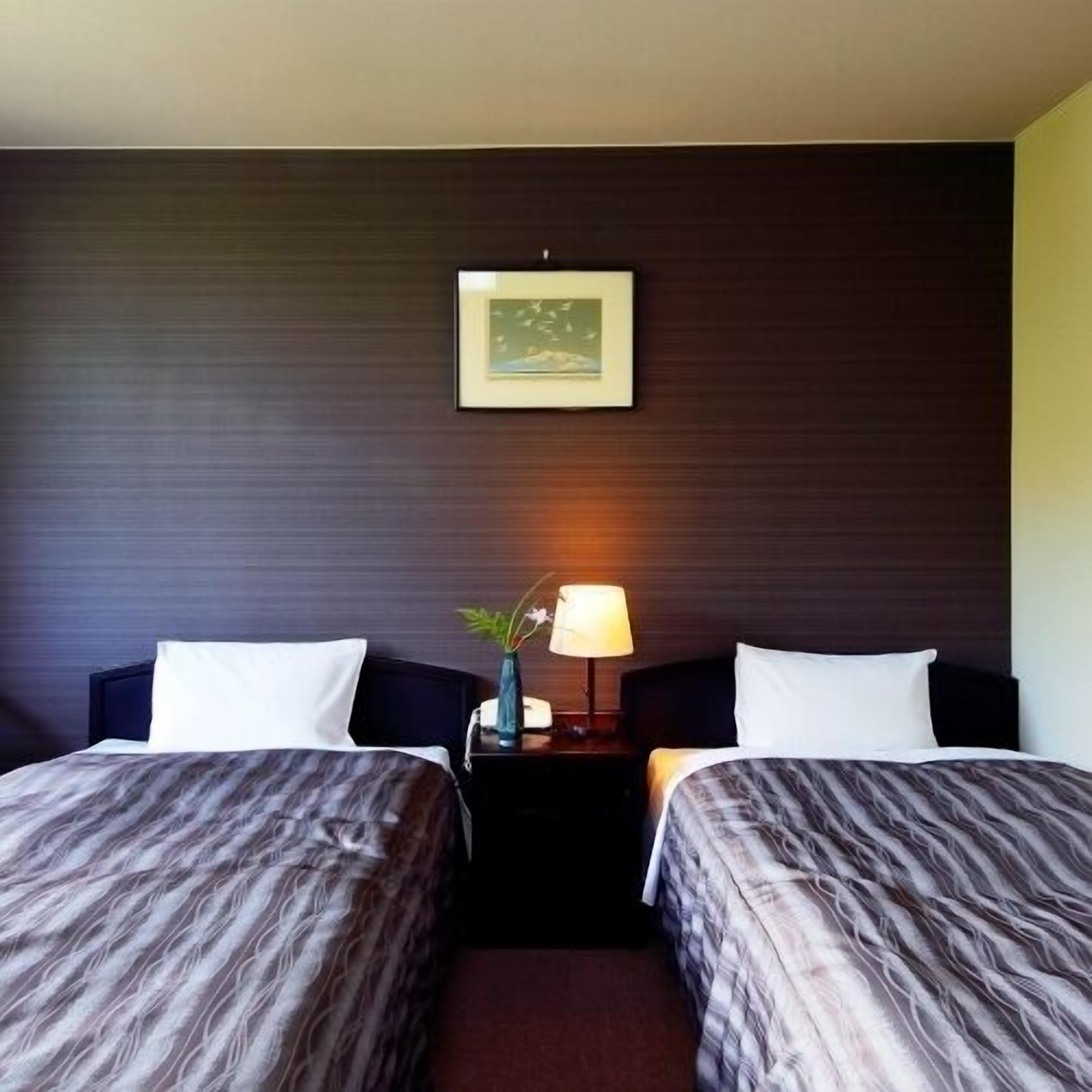 Una camera d'albergo con due letti, un comodino con una lampada e un quadro appeso alla parete.