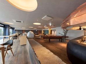 Un interior moderno con mesas y sillas de madera, una gran roca como pieza central y una zona de cocina con detalles en cobre.