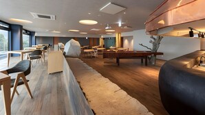 Ein modernes Interieur mit Holztischen und -stühlen, einem großen Felsen als Mittelpunkt und einer Küche mit Kupferdetails.