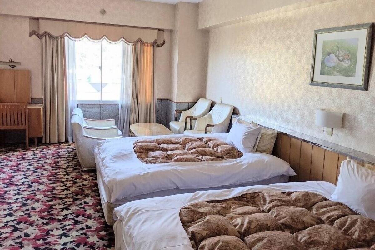 Una habitación de hotel con dos camas, un escritorio, una silla y una ventana con cortinas.