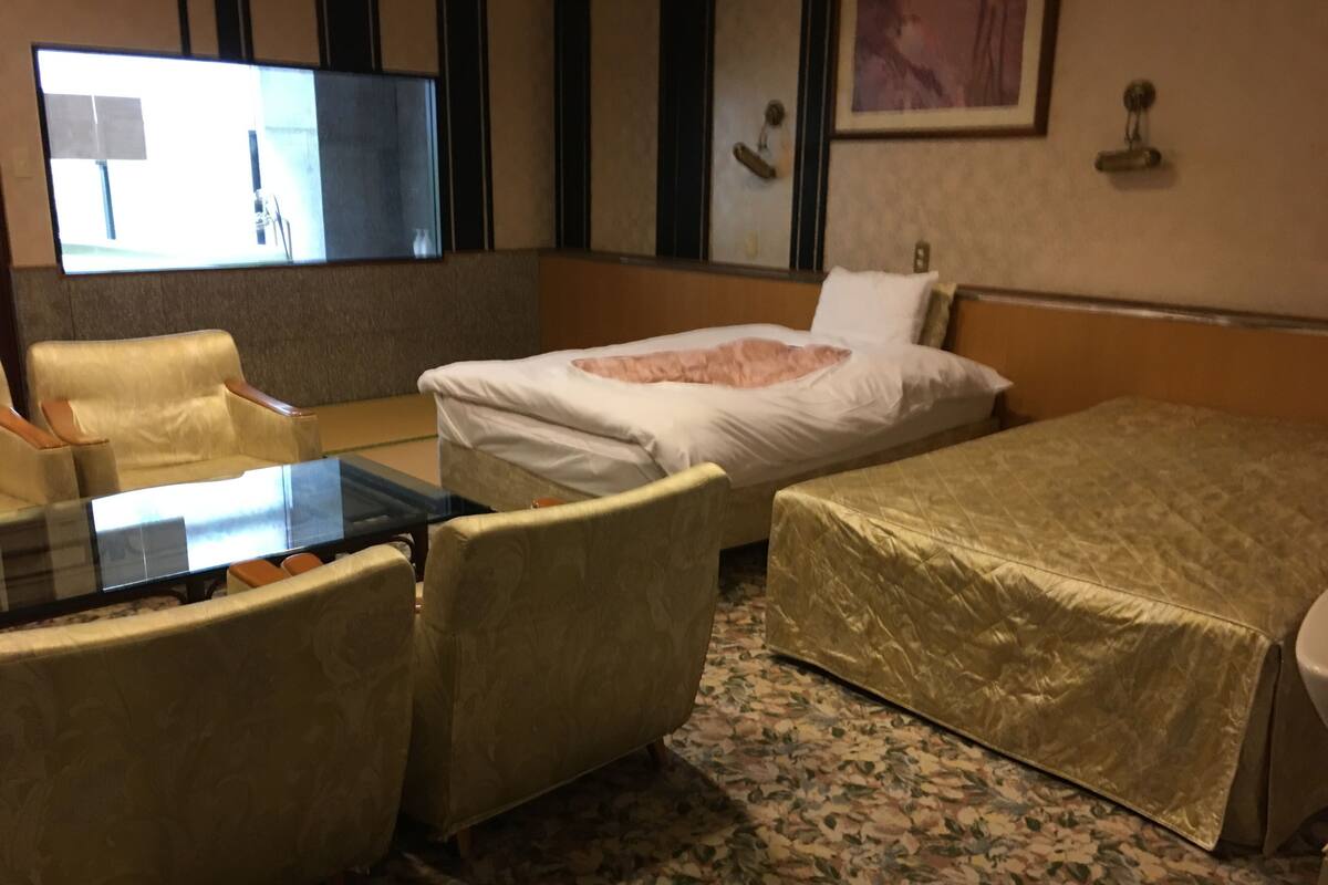 Habitación de hotel con cama, escritorio, dos sillas, una mesita y televisor.