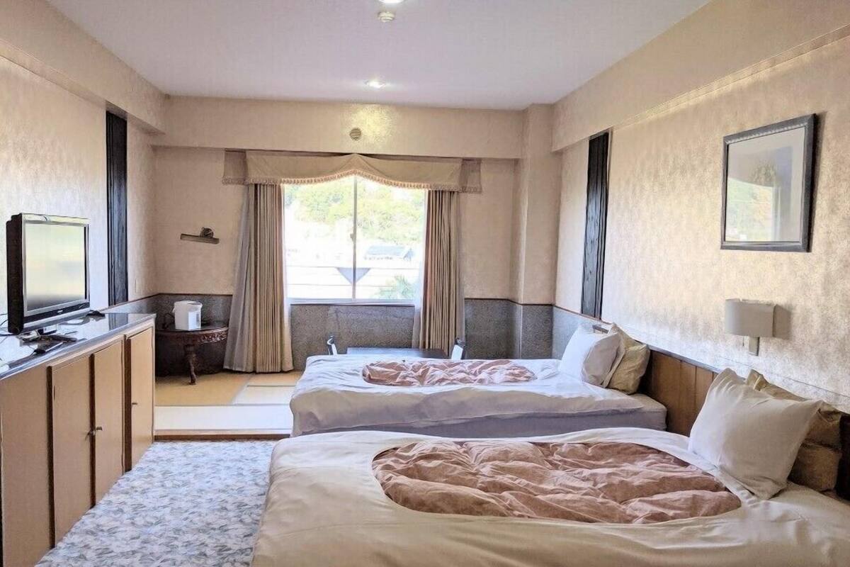 Habitación de hotel con dos camas, televisión, escritorio y ventana con cortinas.