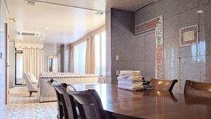 A hotel room with a large round table, several chairs, a sofa, and a view of the cityscape through the windows. - Harazuru Onsen Hotel Topmega Itoen (Asakura)